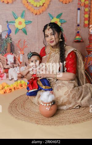 Janmashtami-Konzept. Mutter sitzt mit ihrem süßen Jungen, der als kleine krishna verkleidet ist. Stockfoto