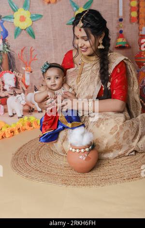 Janmashtami-Konzept. Mutter sitzt mit ihrem süßen Jungen, der als kleine krishna verkleidet ist. Stockfoto