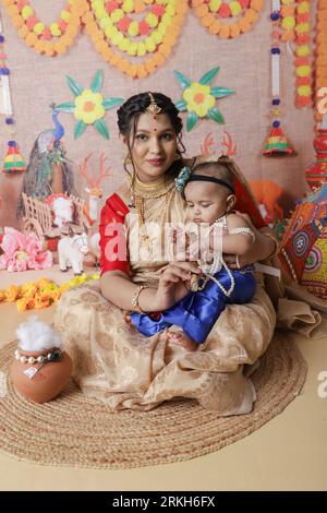 Janmashtami-Konzept. Mutter sitzt mit ihrem süßen Jungen, der als kleine krishna verkleidet ist. Stockfoto