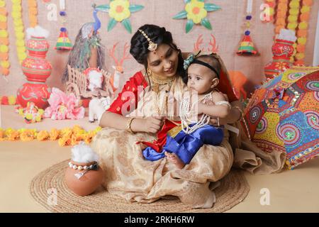 Janmashtami-Konzept. Mutter sitzt mit ihrem süßen Jungen, der als kleine krishna verkleidet ist. Stockfoto