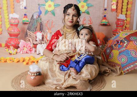 Janmashtami-Konzept. Mutter sitzt mit ihrem süßen Jungen, der als kleine krishna verkleidet ist. Stockfoto