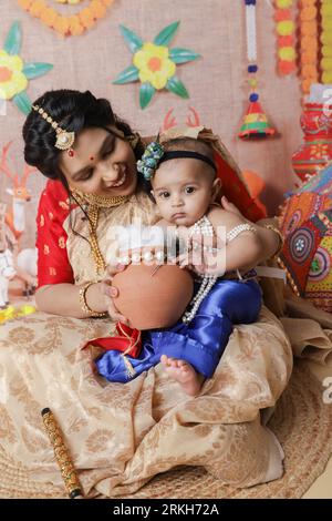 Janmashtami-Konzept. Mutter sitzt mit ihrem süßen Jungen, der als kleine krishna verkleidet ist. Stockfoto