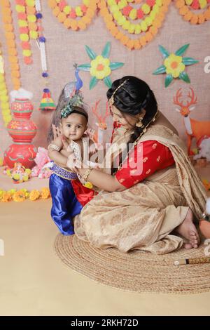 Janmashtami-Konzept. Mutter sitzt mit ihrem süßen Jungen, der als kleine krishna verkleidet ist. Stockfoto