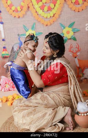 Janmashtami-Konzept. Mutter sitzt mit ihrem süßen Jungen, der als kleine krishna verkleidet ist. Stockfoto