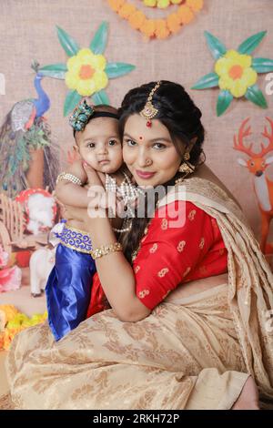 Janmashtami-Konzept. Indische Mutter sitzt mit ihrem süßen Jungen, der als kleine krishna verkleidet ist. Stockfoto