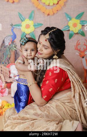 Janmashtami-Konzept. Indische Mutter sitzt mit ihrem süßen Jungen, der als kleine krishna verkleidet ist. Stockfoto