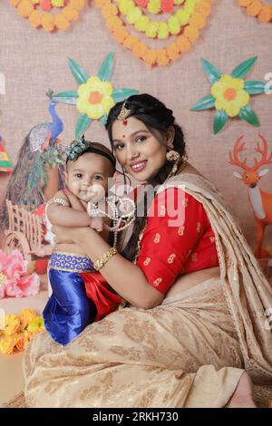 Janmashtami-Konzept. Mutter sitzt mit ihrem süßen Jungen, der als kleine krishna verkleidet ist. Stockfoto