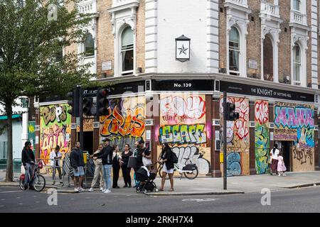 London, Großbritannien. 25. August 2023. Vor dem Notting Hill Carnival kommen die Menschen an einem Pub vorbei, denn Europas größtes Straßenfest, das die karibische Kultur feiert, soll täglich über 1 Million Menschen willkommen heißen. Es wurde auch berichtet, dass Kensington und Chelsea Council ein Wochenende für 41 ältere und gefährdete Erwachsene finanziert haben, die auf der Karnevalsroute leben und während der Feierlichkeiten möglicherweise Schwierigkeiten haben, ihre Immobilien zu verlassen Stockfoto