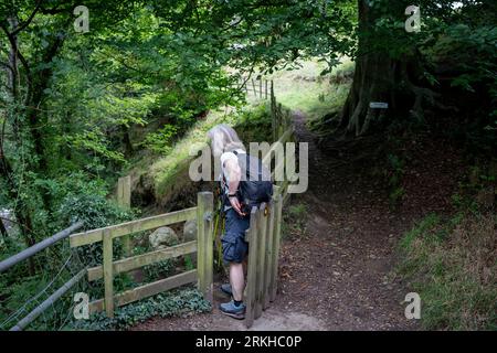 A woman walker squeezes through a gate on a footpath at Edale in the Peak District National Park, on 24th August 2023, in Sheffield, England. Stock Photo