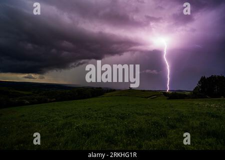 A striking purple lightning bolt illuminates a turbulent dark sky on a cloudy evening Stock Photo