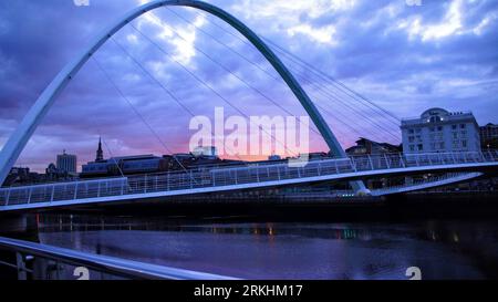 The Gateshead Millennium Bridge illuminated in a warm orange light at a tranquil sunset Stockfoto