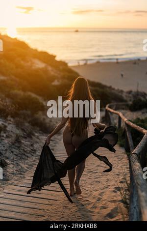 Eine Frau, die auf einem Strandweg spaziert, der von den Orange- und Rosatönen eines malerischen Sonnenuntergangs erleuchtet wird. Stockfoto