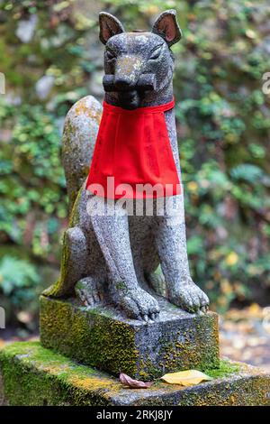 Eine Statue eines Fuchses (in japanischem Kitsune) mit einem roten Lätzchen, am Fushimi Inari-Schrein in Kyoto, Japan. Füchse werden als Boten des Gottes Inari angesehen. Stockfoto