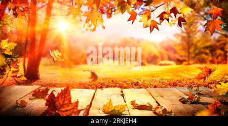Herbst – Holztisch Mit Fallenden Orangenblättern Bei Sonnenuntergang Im Park Mit Abstrakten, Unscharfen Lichtern Stockfoto