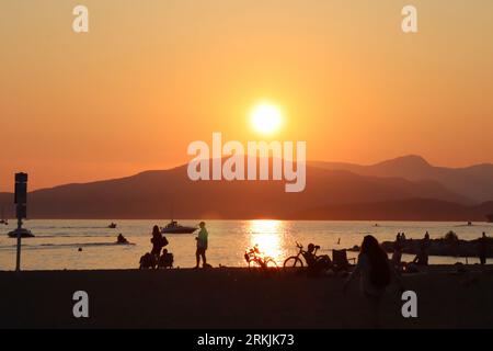 Eine große Gruppe von Menschen versammelte sich am Strand, mit Blick auf den Sonnenuntergang Stockfoto