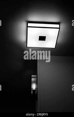 Schwarz-weiß-Bild, das auf eine Leuchte an Decke und Wand in einem Hotelzimmer schaut. Stockfoto
