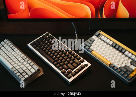 A computer with three different mechanical keyboards lying on the desk next to the monitor Stock Photo