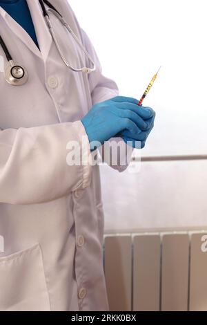 Unbekannter Arzt in blauen Handschuhen, weißem Mantel und Stethoskop mit einer Spritze in der Hand Stockfoto