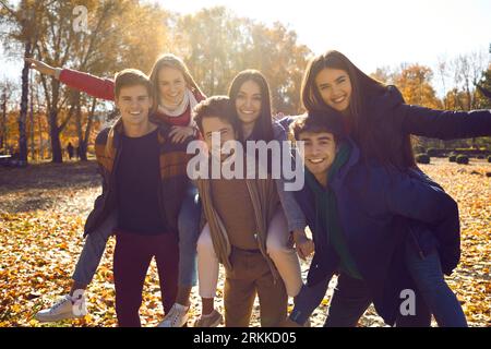 Gruppe junger Menschen, die ihre Mädchen beim Spaziergang in einem sonnigen Herbstpark begleiten Stockfoto