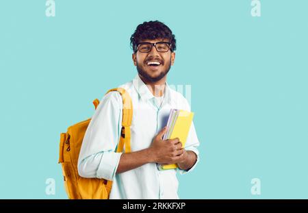 Junger glücklicher indischer Student mit Rucksack und Büchern in den Händen, die sich über den Eintritt in die Universität freuen Stockfoto