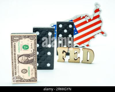Dollar-Banknote auf Dominosteinen mit eingefügtem Dominostück und US-Flagge auf weißem Hintergrund, Konzept der Finanzkrise Stockfoto