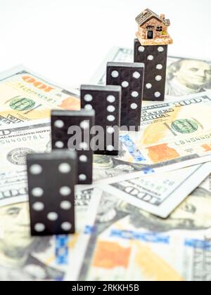 Mini-Haus auf Domino auf Dollar-Banknoten, Krisenkonzept Stockfoto