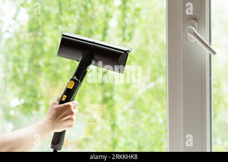 Eine Frau wäscht die Fenster eines Hauses mit einer Dampfbügelstation. Um im Frühling das Haus aufzuräumen. Hausreinigung. Selektiver Fokus. Stockfoto