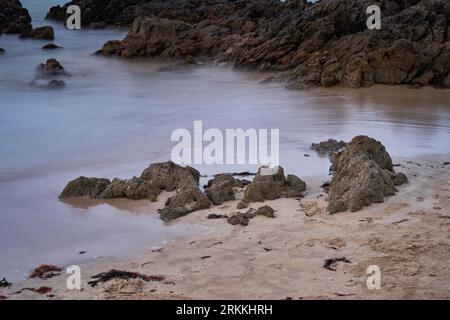 Lange Exposition der Felsen am Strand mit einem bedeckten Himmel Stockfoto