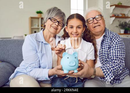 Glückliches Enkelkind zusammen mit Großmutter und Großvater spart Geld in der Schweinebank Stockfoto