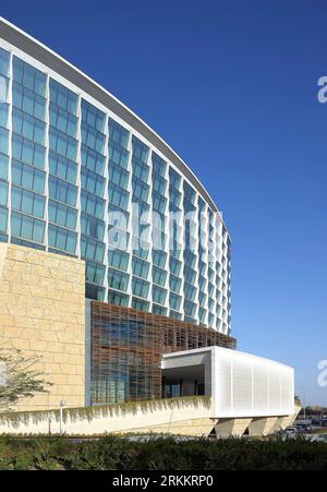 Geschwungene Fassade mit Verglasung und Steinverkleidung. 360 Mall, Kuweit City, Kuwait. Architekt: CRTKL, 2021. Stockfoto