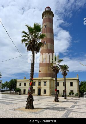 Leuchtturm (Farol de Aveiro) am Strand Praia da Barra, Palmen mit Kabeln, um sie gegen den Wind zu halten, Aveiro, Portugal Stockfoto