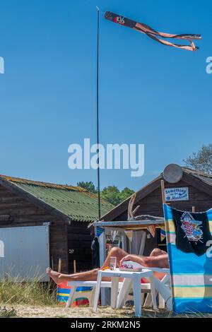 Zusammenfassung. Mann sonnt sich die Beine und entspannt sich vor einem typischen British Beach Hütten in Dorset. UK. Sommer. Sonnig. Keine Fläche wird angezeigt. Klassisch Britisch. Stockfoto