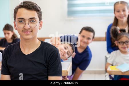 Die Schulkinder, die stehen, bebeißen sich gegenseitig, während sie lächeln Stockfoto