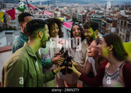 Gruppe von jungen erwachsenen Freunden, die Spaß beim Toasten und Trinken von alkoholischen Gläsern haben. Auf einer abendlichen Party auf dem Dach können sich viele Menschen mit Bier, Getränken und Cocktails treffen. Hochwertige Fotos Stockfoto