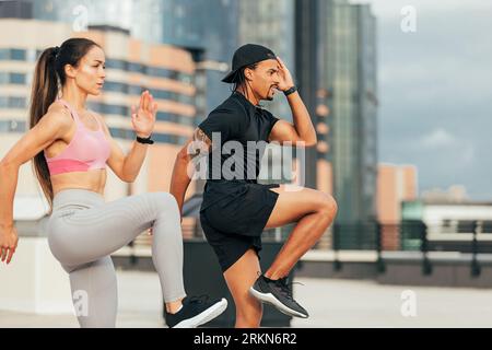 Young athletes are exercising together on rooftop. Man and woman are warming up before training outdoors. Stockfoto