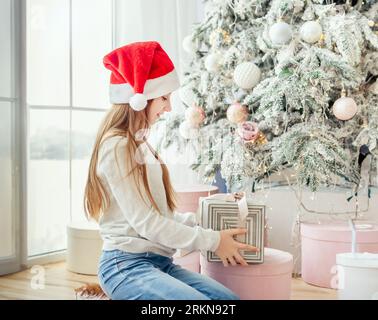 Teenager-Mädchen in santa hat offenes Geschenk in der Nähe von weihnachtsbaum Stockfoto