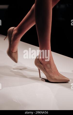 Weibliche Beine beigefarbene High Heels, die die Modenschau auf dem Laufsteg begleiten. Stylische vertikale Modeshots Stockfoto