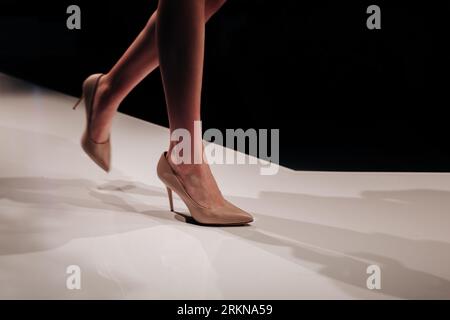 Weibliche Beine beigefarbene High Heels, die die Modenschau auf dem Laufsteg begleiten. Stylische, minimalistische Modeshots Stockfoto
