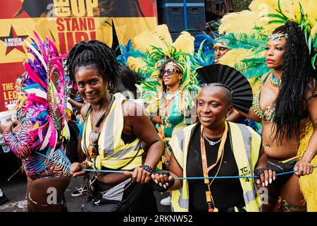 Zwei Freiwillige werden gesehen, wie sie die Künstler bei der Veranstaltung schützen. Nach zwei Jahren Pandemie, der größten Straßenparty in Europa, kehrte Notting Hill Carnival 2022 zurück und war der 54. Karneval seit 1966. Es wird erwartet, dass es 2 Millionen Teilnehmer am Karneval sowie 40.000 Freiwillige und 9.000 Polizisten gibt. Stockfoto