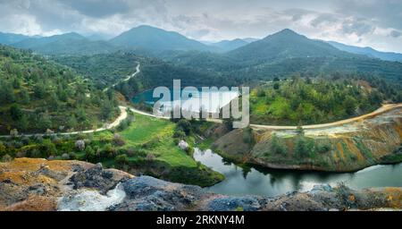 Wiederherstellung von verlassenen Bergbaugebieten in Zypern. Panorama der Tagebaugrube Memi Sulfides Mine mit Grubensee und bunten Bergwerksrückständen im Vordergrund Stockfoto