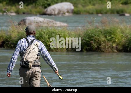 Der Mann geht mit seiner Angelrute und seiner ganzen Ausrüstung an einem Fluss entlang. Stockfoto