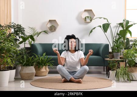 Entspannende Atmosphäre. Frau meditiert in der Nähe von Zimmerpflanzen im Zimmer Stockfoto