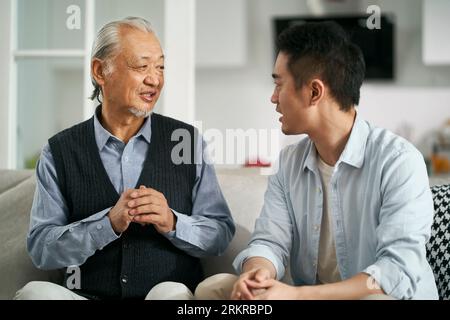 Senior-asiatischer Vater hat sich zu Hause auf der Couch amüsiert und sich mit dem erwachsenen Sohn unterhalten Stockfoto