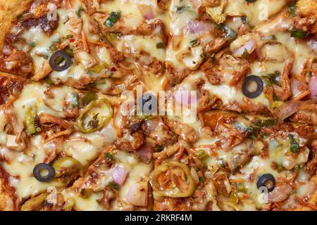 Nahaufnahme von scharfer Hühnerpizza, frisch zubereiteter Pizza, gemischt mit gegrilltem Gemüse, Oliven und doppelten Lagen Mozzarella-Käse, mit Strei Stockfoto