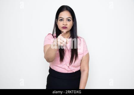 Junge indische Geschäftsfrau, die mit dem Finger auf die Kamera zeigt, mit ernsthaftem Ausdruck auf ihrem Gesicht isoliert über weißem Hintergrund, wütender Manager oder Manager. Stockfoto