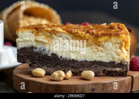Käsekuchen mit Schokoladenschwammkuchen und Erdnüssen in Karamell, köstliches Dessert mit Erdnüssen und Käsesahne Stockfoto