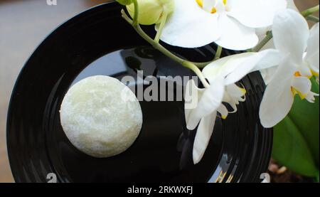 Traditionelles japanisches Dessert Wagashi Mochi Rise Kuchen weiß auf schwarzem Teller mit Blumen dekoriert. Food-Fotografie, Nahaufnahme, flach liegen Stockfoto