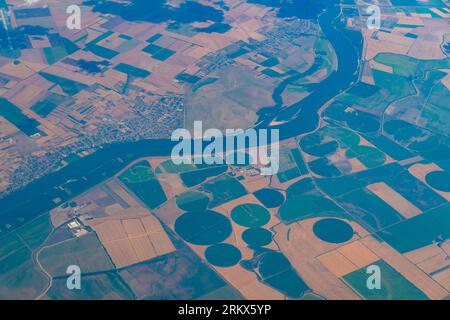 Luftaufnahme der Bewässerung mit Mittelzapfen, bei der sich die Ausrüstung um einen Zapfen dreht und die Pflanzen in Europa mit Sprinklern mit dem Fluss bewässert werden. Stockfoto