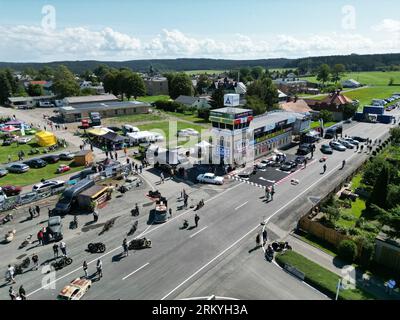 Schleiz, Deutschland. 26. August 2023. Bei der Eröffnung der Motorwelt „Schleizer Dreieck“ laufen die Besucher durch die Ausstellungsfläche. Der Schleizer Dreieck ist Deutschlands älteste Strassenbahn und auch heute noch Austragungsort von Motorsportrennen. Das Museum ist der hundertjährigen Geschichte der Rundstrecke gewidmet. (Gedreht mit Drohne) Credits: Bodo Schackow/dpa/Alamy Live News Stockfoto