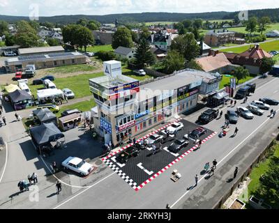 Schleiz, Deutschland. 26. August 2023. Bei der Eröffnung der Motorwelt „Schleizer Dreieck“ laufen die Besucher durch die Ausstellungsfläche. Der Schleizer Dreieck ist Deutschlands älteste Strassenbahn und auch heute noch Austragungsort von Motorsportrennen. Das Museum ist der hundertjährigen Geschichte der Rundstrecke gewidmet. (Gedreht mit Drohne) Credits: Bodo Schackow/dpa/Alamy Live News Stockfoto